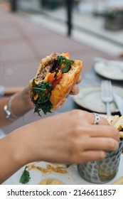 Woman Holding Half Eaten Burger In One Hand And Eating French Fries With The Other Hand