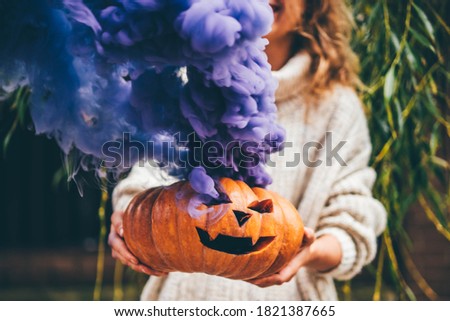 Woman holding Halloween pumpkin. Halloween orange pumpkin smoking with purple smoke. 