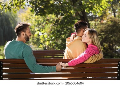 Woman Holding Hands With Another Man Behind Her Boyfriend's Back On Bench In Park. Love Triangle