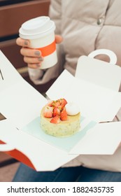 Woman Is Holding In Hands An Appetizing Cake With Strawberries And And Hot Beverage Bought In Restaurant For Takeaway. Eating Outdoors In The Park. Social Distance During The Pandemic And Closed Cafes