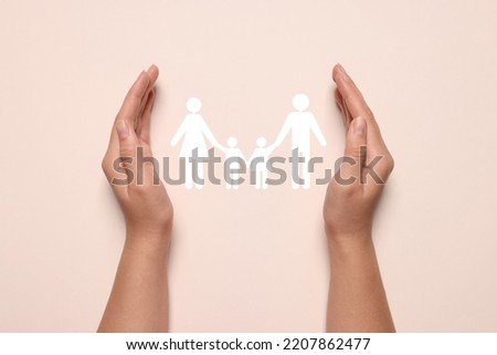 Woman holding hands around paper silhouette of family on light pink background, top view. Insurance concept
