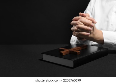 Woman Holding Hands Clasped While Praying At Table With Bible Against Black Background, Closeup. Space For Text