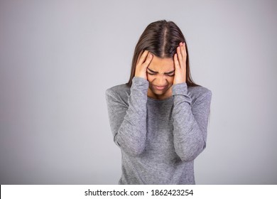Woman holding hands to her temples having terrible headache. Studio shot on grey wall.  Woman has a terrible headache, isolated on white wall. Studio shot