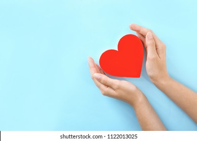 Woman holding hands near red heart on color background, top view