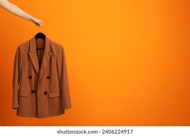 Woman holding hanger with stylish jacket on orange background, closeup. Space for text