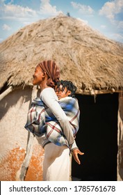 Woman Holding Her Daughter, In The Back In A Blanket,  African Family In Botswana Village