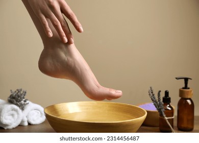 Woman holding her foot over bowl with water, closeup. Pedicure procedure
