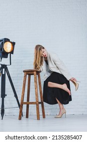 A Woman Is Holding Her Leg She Is Wearing High Heeled Shoes And Her Legs Hurt. The Woman Is Wearing A Black Dress And Beige High Heel Shoes. Leg Pain From High Heels