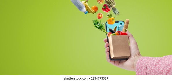 Woman holding her smartphone and doing online grocery shopping, she is receiving fresh food and drinks - Powered by Shutterstock