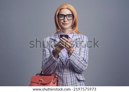 Woman holding her smartphone and staring at camera with a funny expression