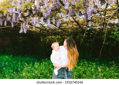 Woman is holding her toddler under a wysteria tree