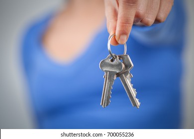 Woman holding home keys in front of her body. Focus on foreground