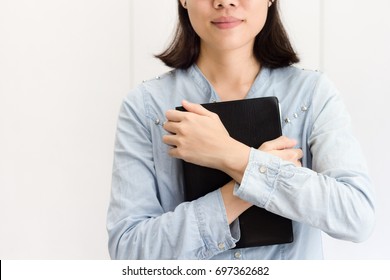 A Woman Is Holding And Hug The Bible At Her Chest In The Morning. Bible Is Black Cover. Gray And White Background.