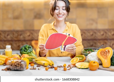 Woman Holding Human Liver Model With Variety Of Healthy Fresh Food On The Table. Concept Of Balanced Nutrition For Liver Health