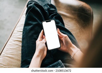 Woman Holding IPhone 13 Pro With A White Screen Mock Up, Resting On A Sofa In Living Room At Home. Rostov-on-Don, Russia - January 6 2022