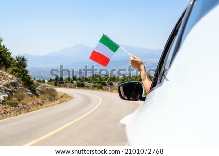 Woman holding  Italy flag from the open car window driving along the serpentine road in the mountains. Concept