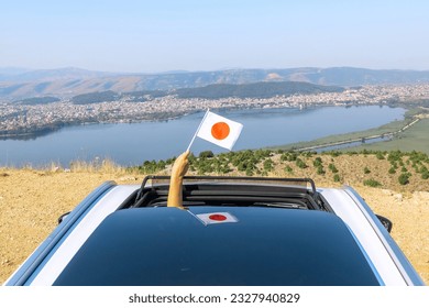 Woman holding Japan flag from the open car sunroof,  window driving along the serpentine road in the mountains. Top view.  Concept