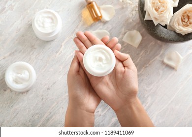 Woman holding jar with body cream over light table