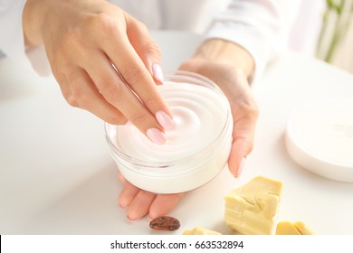 Woman holding jar with cocoa butter lotion over table