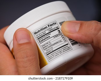 A Woman Holding A Jar With Gums And Reading A Nutrition Facts Label At The Back.