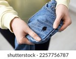 Woman holding jeans with black ink stain on blurred background, closeup