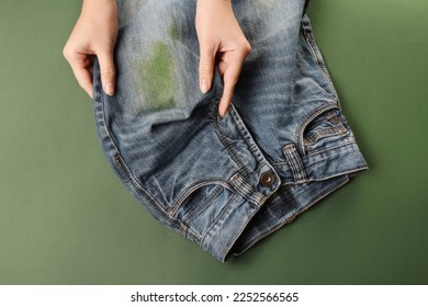 Woman holding jeans with stain on green background, top view - Shutterstock ID 2252566565