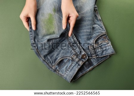 Woman holding jeans with stain on green background, top view