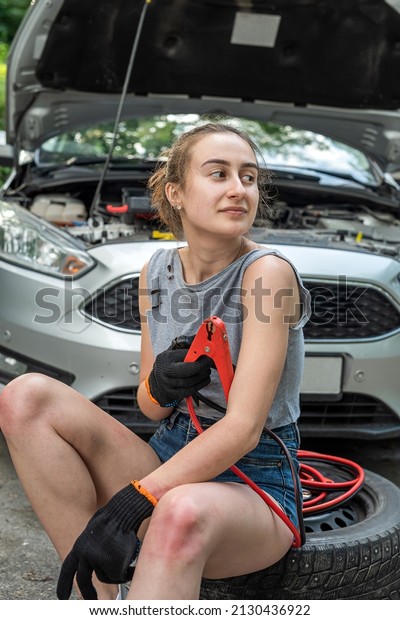 woman holding  jumper\
cable for recharge the battery car for repairing broken car.\
service at outdoor