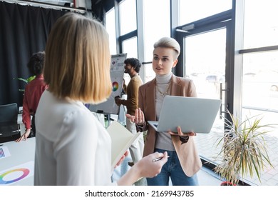 Woman Holding Laptop During Conversation With Blurred Colleague In Ad Agency