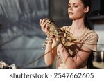 Woman holding a large lobster in front of a kitchen, seafood preparation concept