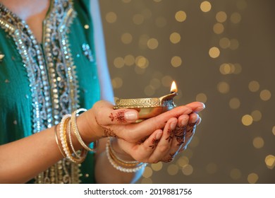 Woman holding lit diya lamp on brown background with blurred lights closeup view. Diwali holiday