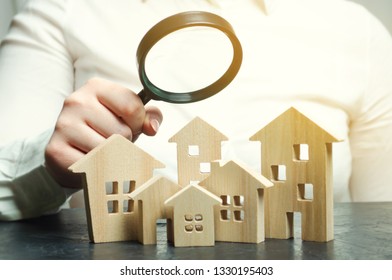 A woman is holding a magnifying glass over a wooden houses. Real estate appraiser. Property valuation / appraisal. Find a house. Search for housing. Real estate market analysis. Selective focus