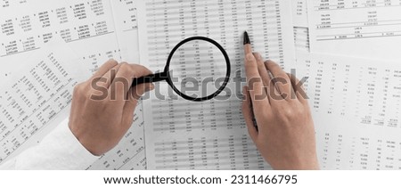 Woman holding a magnifying glass pointing at numbers on financial documents. ?oncept of finance, search and accounting.