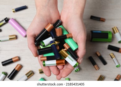 Mujer sosteniendo muchas baterías eléctricas usadas en sus manos sobre mesa blanca, cerrando