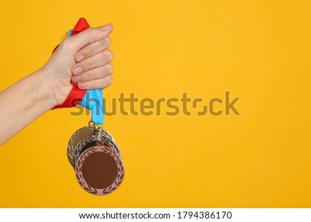 Woman holding medals on yellow background, closeup. Space for design