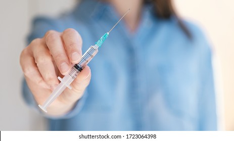 Woman holding medical injection syringe in her outstretched hand towards the camera. Selective focus, copy space
