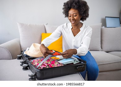 Woman holding medical mask against suitcase with packed clothes and straw hat.Planning a summer trip in the new normal after lockdown. Suitcase packing for travel, COVID-19