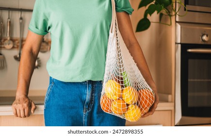 Woman Holding Mesh Bag with Fresh Vegetables in Kitchen.Eco-friendly bag filled with fresh produce held by a person. - Powered by Shutterstock