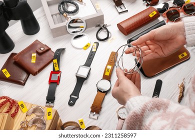 Woman holding metal earrings near table with different stuff, closeup. Garage sale - Shutterstock ID 2311258597