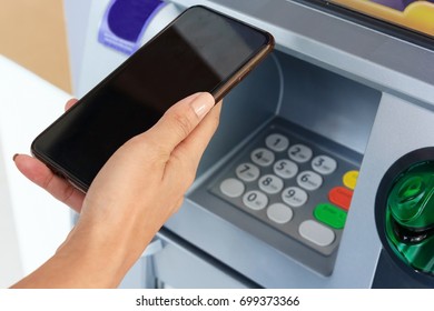 Woman Holding Mobile Phone With Black Screen And A Credit Card At An ATM. Security Code On An Automated Teller Machine