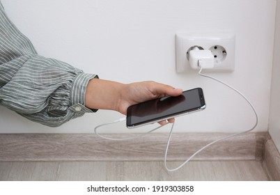 Woman holding mobile phone with connected charger near white brick wall indoors, closeup - Powered by Shutterstock