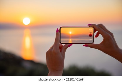 Woman Holding Mobile Phone In Hands And Taking Sunrise Photo