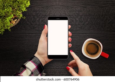 Woman Holding Modern Black Phone With Blank Screen In Hand And Touching Display, Top View. Coffee And Green Plant Placed On Grey Table In Background