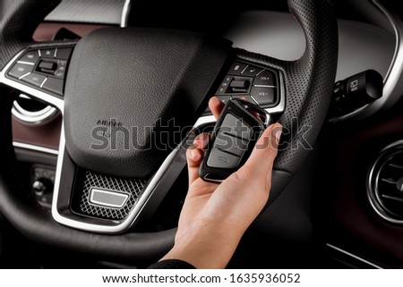 Woman holding modern car key, alarm system and steering wheel with electric buttons - female hands