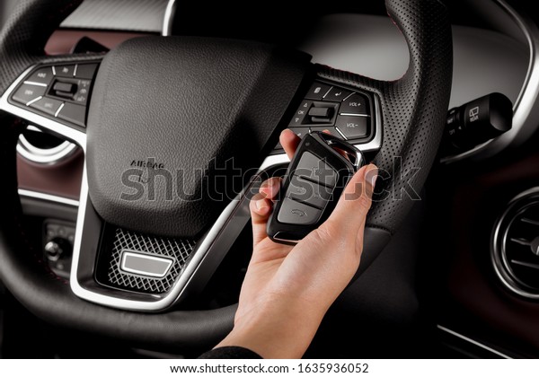 Woman holding modern car\
key, alarm system and steering wheel with electric buttons - female\
hands