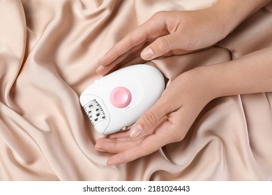 Woman Holding Modern Epilator On Silk Fabric, Top View