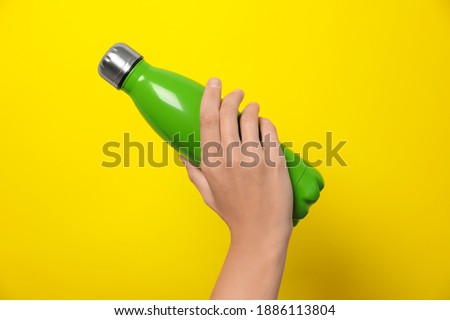 Woman holding modern green thermos on yellow background, closeup