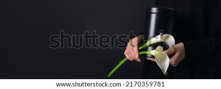 Woman holding mortuary urn and flowers on black background with space for text, closeup