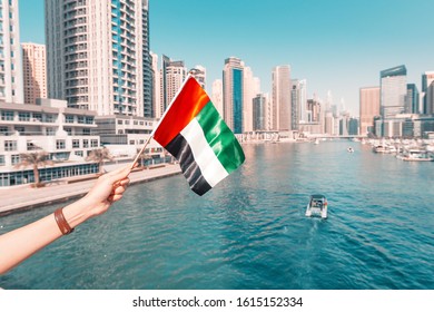 Woman holding national flag of United Arab Emirates, while standing in Marina district of Dubai