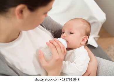 Woman holding a newborn baby in her arms and feeds him from a milk bottle. - Powered by Shutterstock